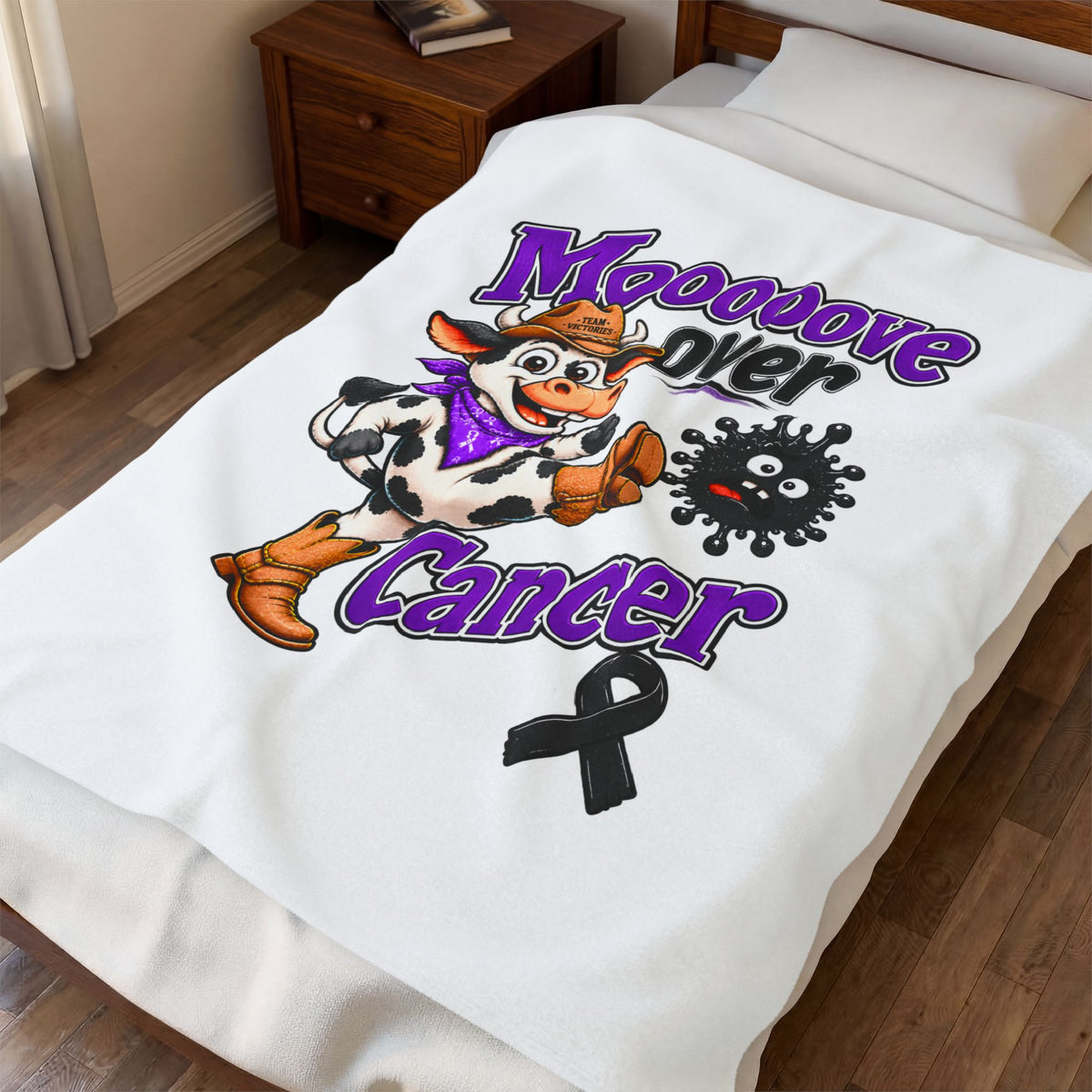 Moooove Over Cancer white plush blanket draped over a bed with cow artwork and black ribbon