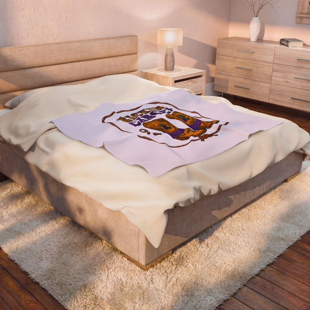 Lavender Kickin' Cancer plush blanket displayed across a bed in a softly lit bedroom