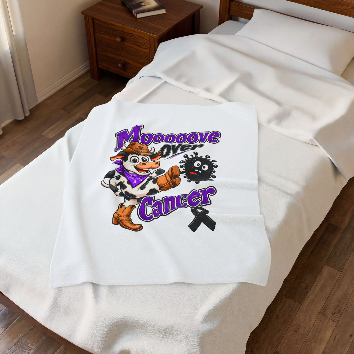 Folded white Moooove Over Cancer blanket on a bed with printed design visible