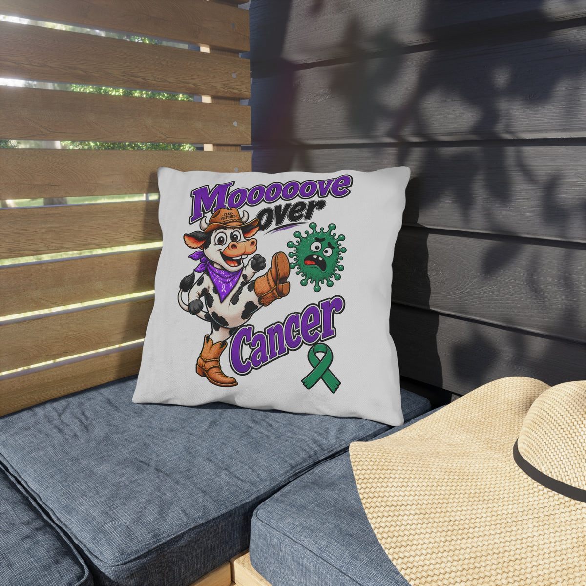 Moooove Over Cancer outdoor pillow on patio seating featuring a cow character and green awareness ribbon