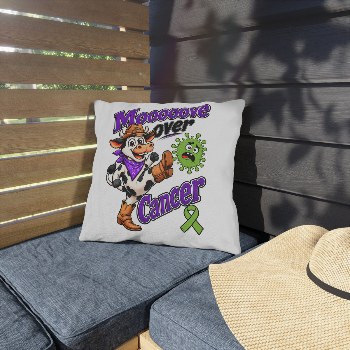 Moooove Over Cancer outdoor pillow on patio seating featuring a cow and green awareness ribbon