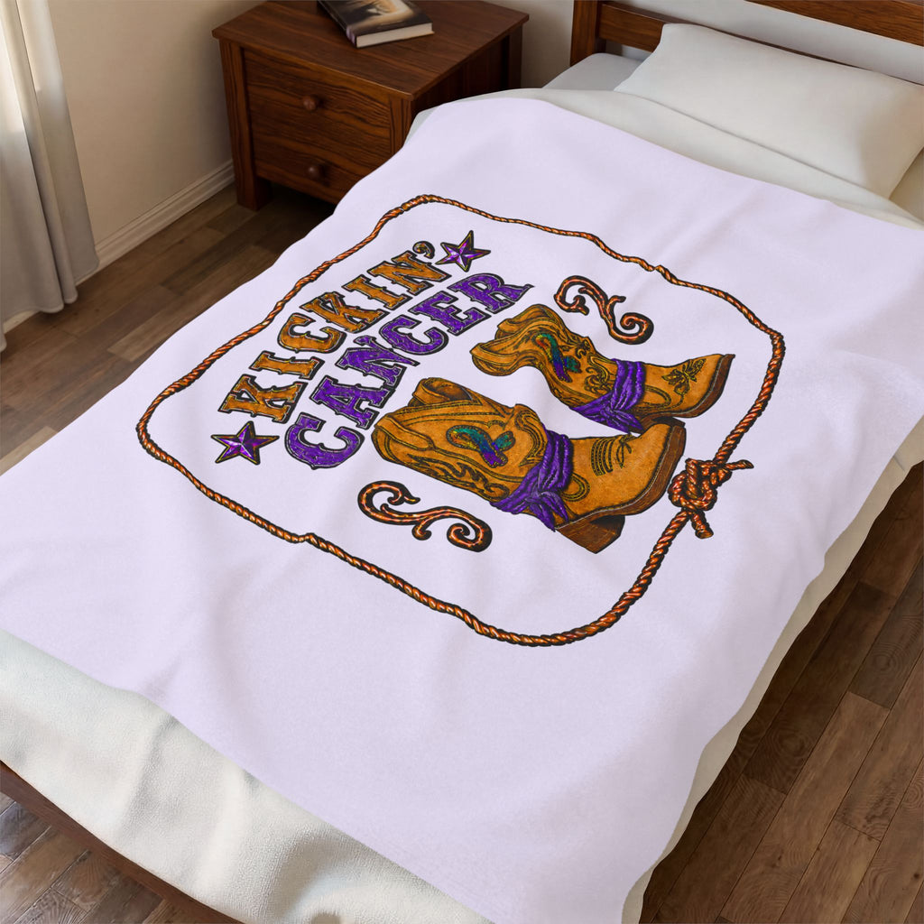 Lavender Kickin' Cancer plush blanket spread across a bed with cowboy boot and awareness artwork
