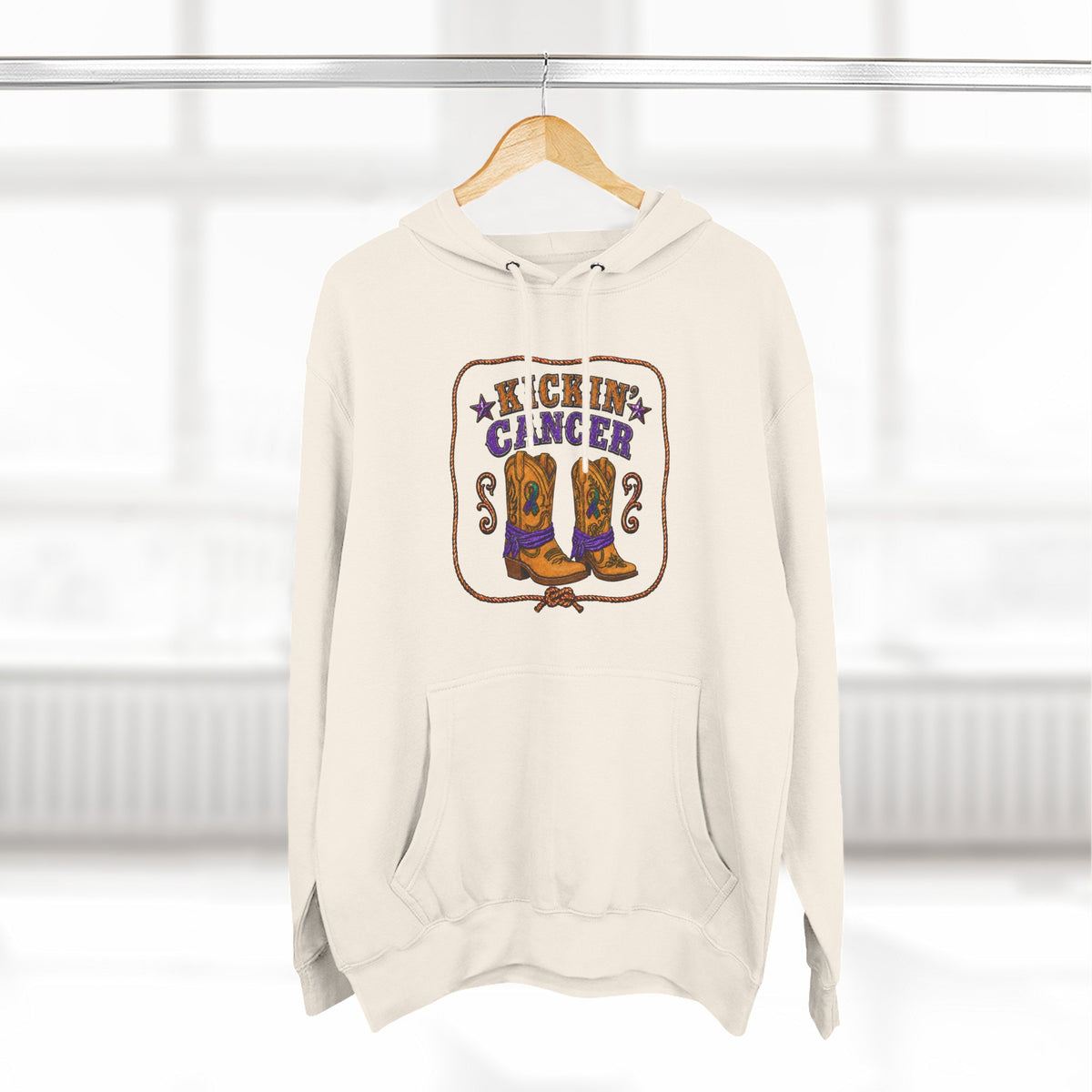 Cream Kickin' Cancer hoodie hanging from a wooden hanger