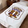 White Kickin' Cancer plush blanket spread on a bed with vertical cowboy boot artwork