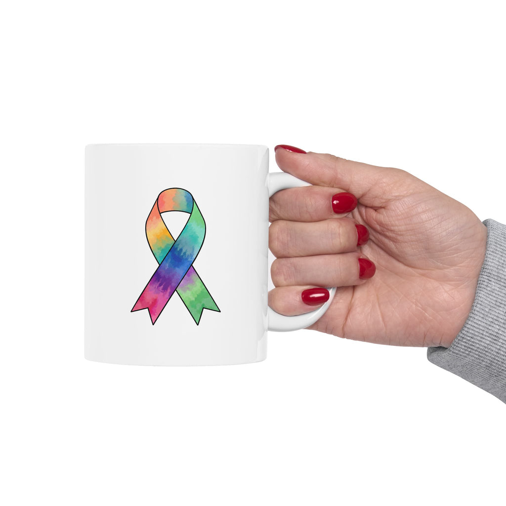 Hand holding a white Kickin’ Cancer mug with awareness ribbon artwork