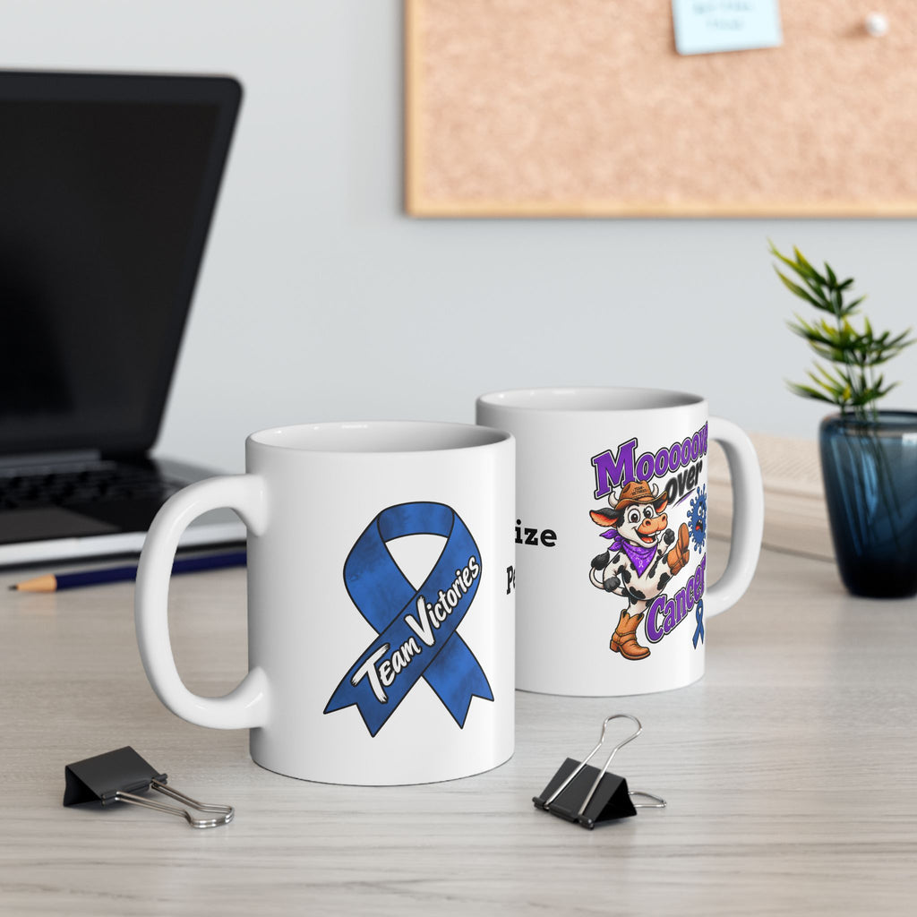 Two Moooove Over Cancer mugs on a desk, showing the cow design and Colon Cancer awareness ribbon