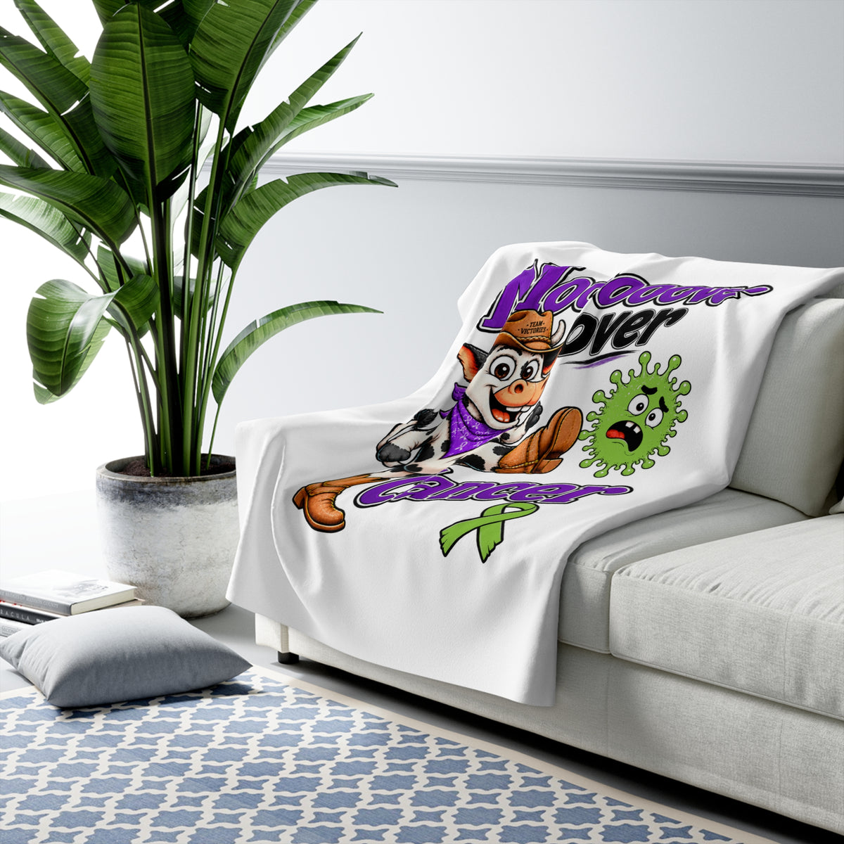 Moooove Over Cancer sherpa blanket draped over a sofa with Non-Hodgkin/Lymphoma Cancer awareness ribbon